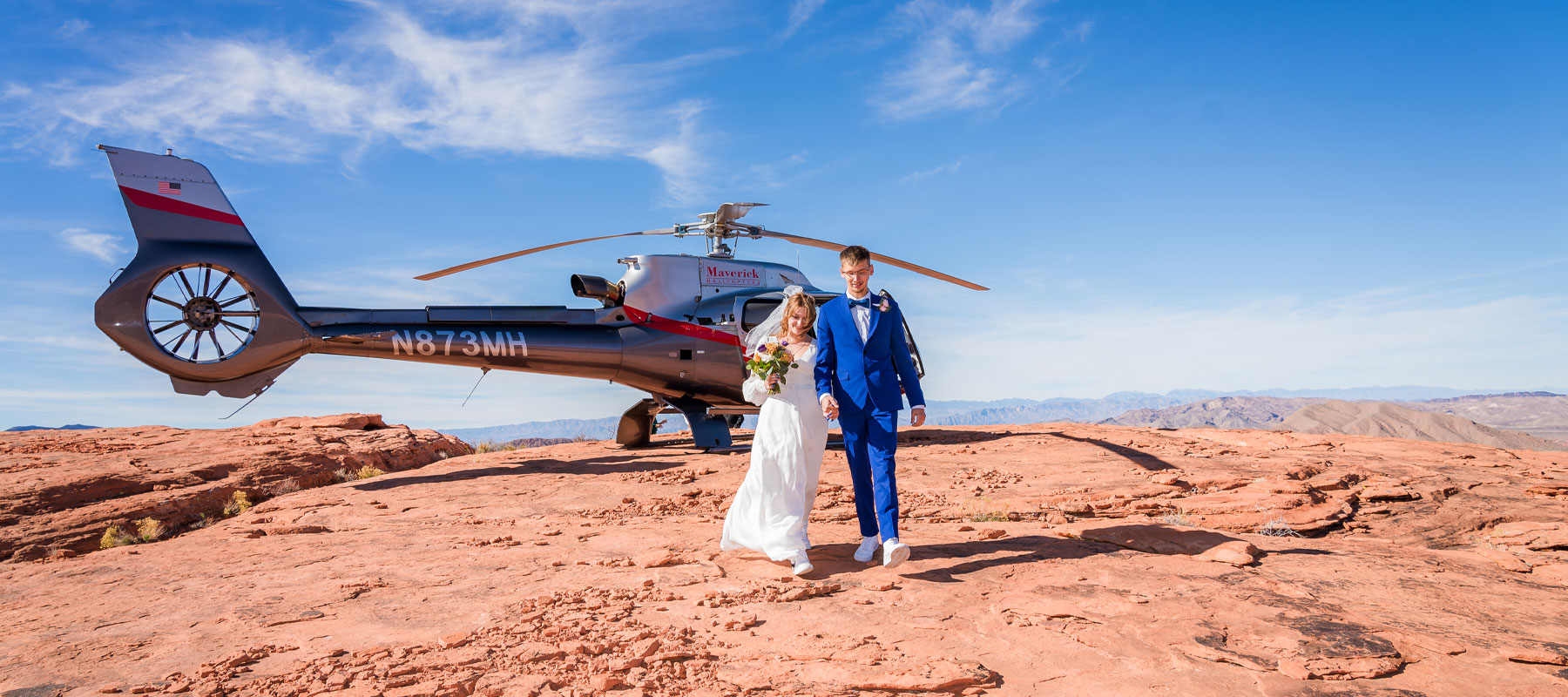 Bride and groom standing together on red sandstone with open blue sky at Valley of Fire